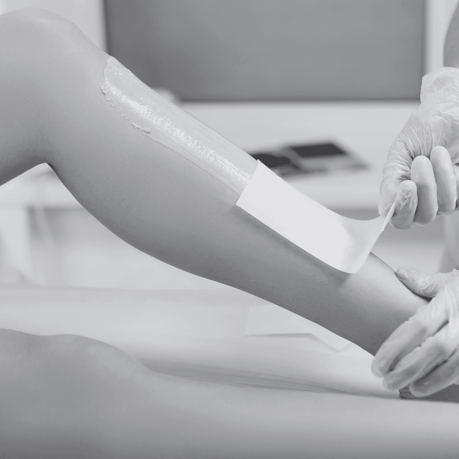Person receiving hair removal treatment on leg with waxing strip in a clinic.