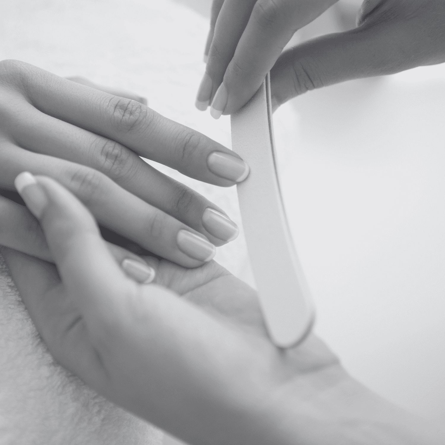 A person receiving a manicure, with focus on nail filing by a professional.