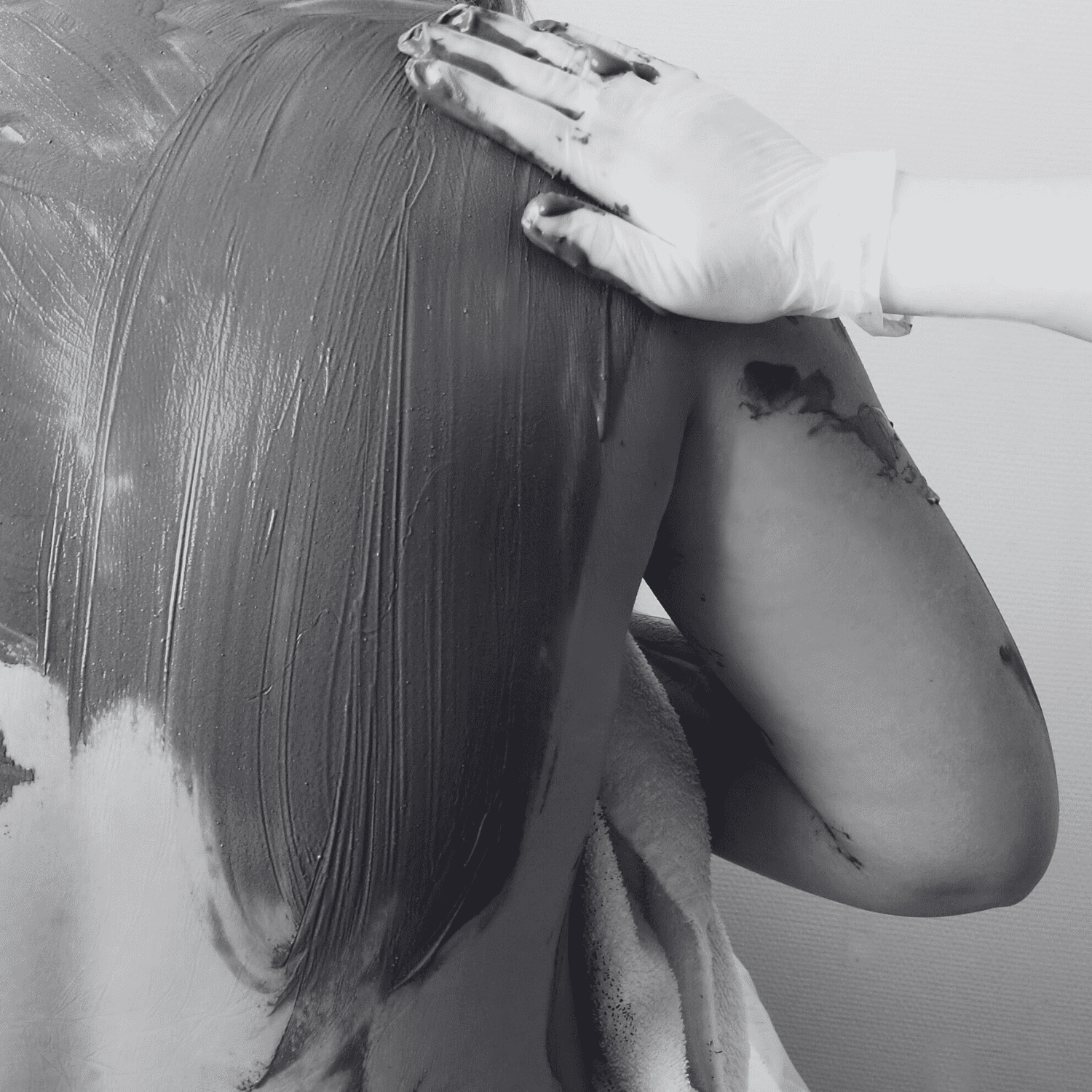 Person receiving a therapeutic mud treatment on their back, close-up of hands applying mud.