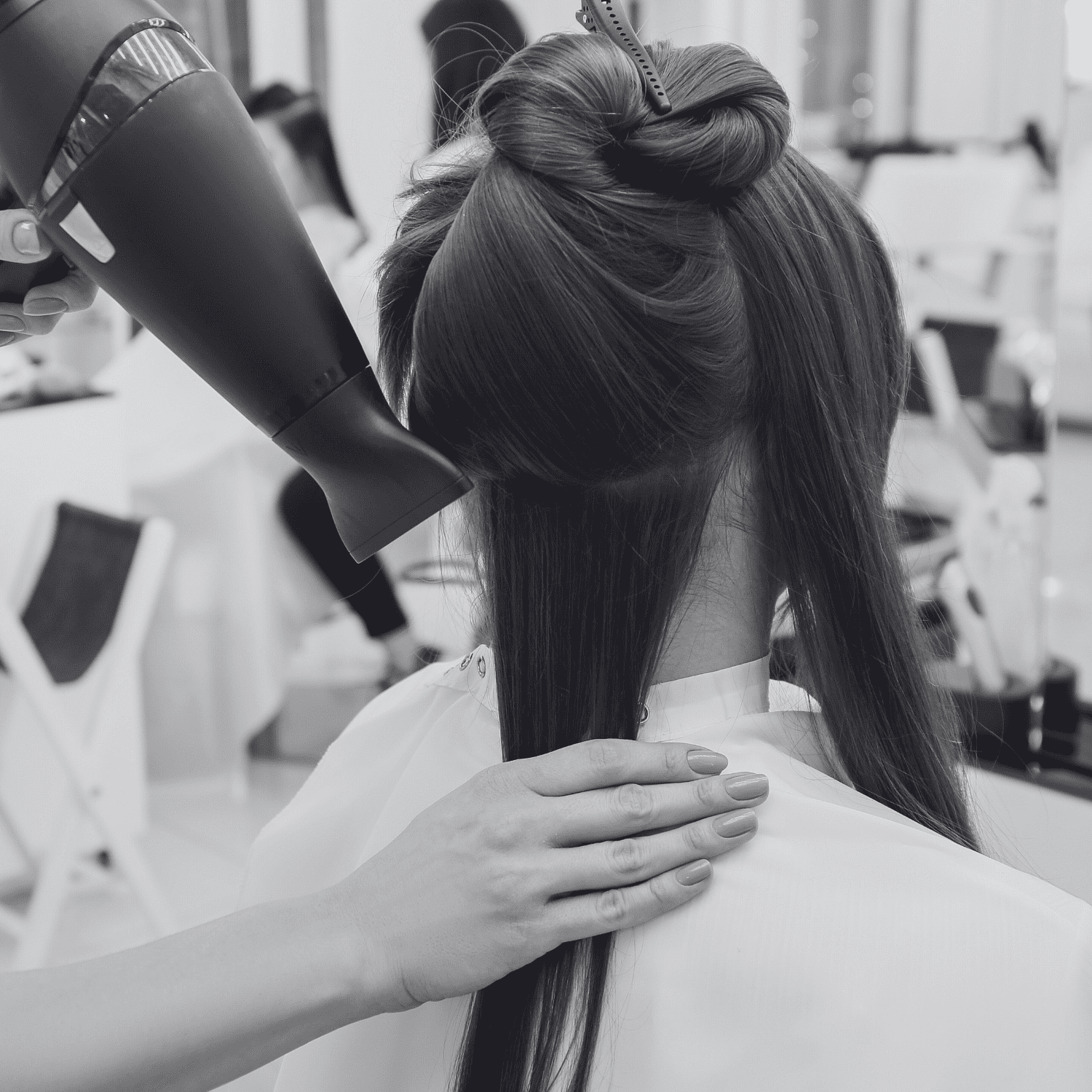 Hairdresser blow-drying a woman's hair in a salon.