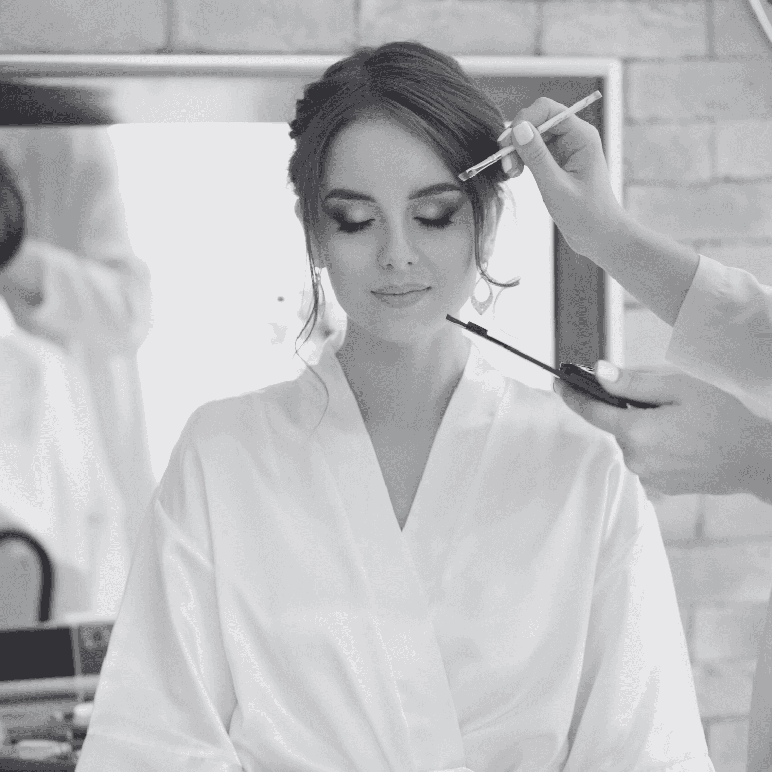 Woman in white robe getting her makeup done with a brush in front of a mirror.