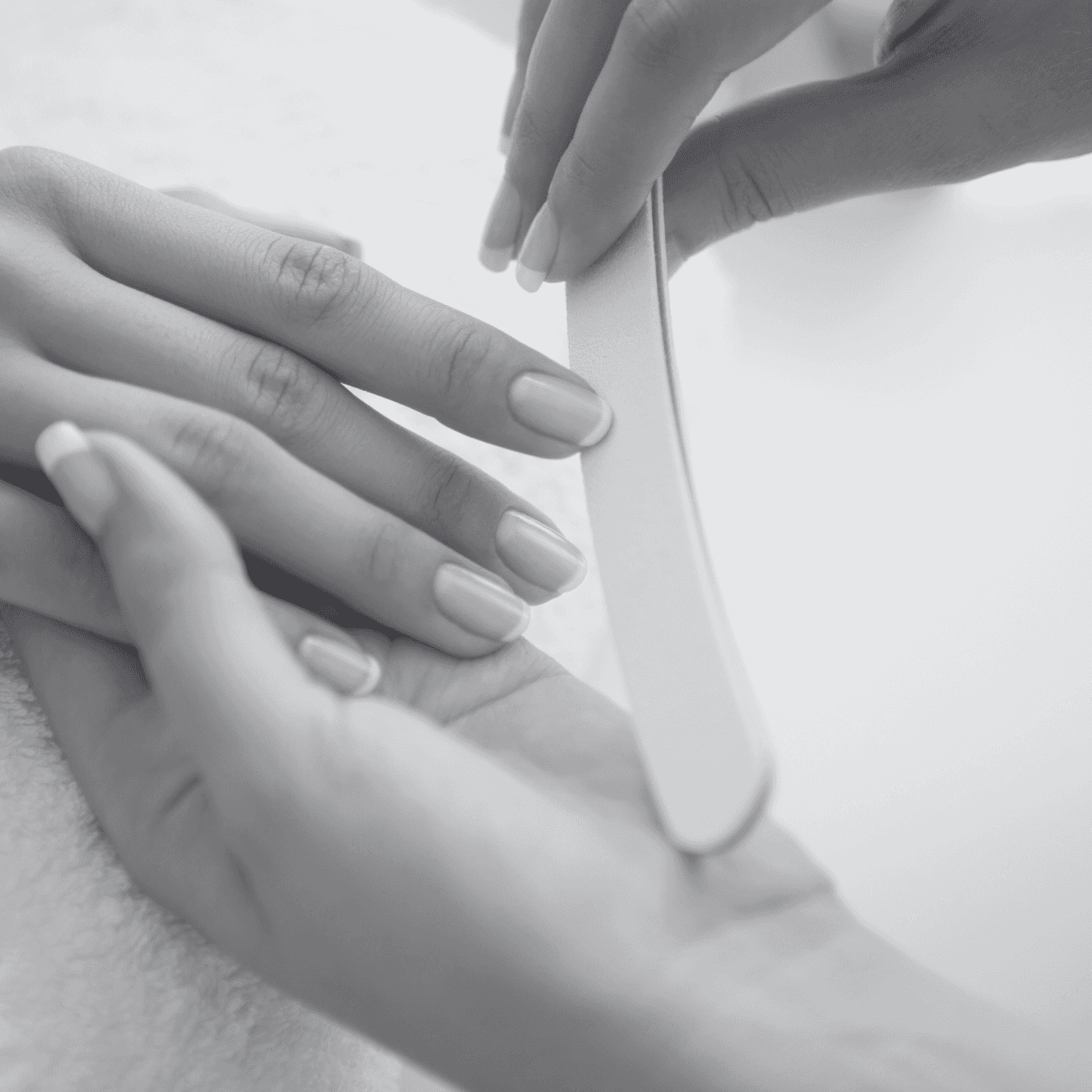 A person receiving a manicure, with focus on nail filing by a professional.
