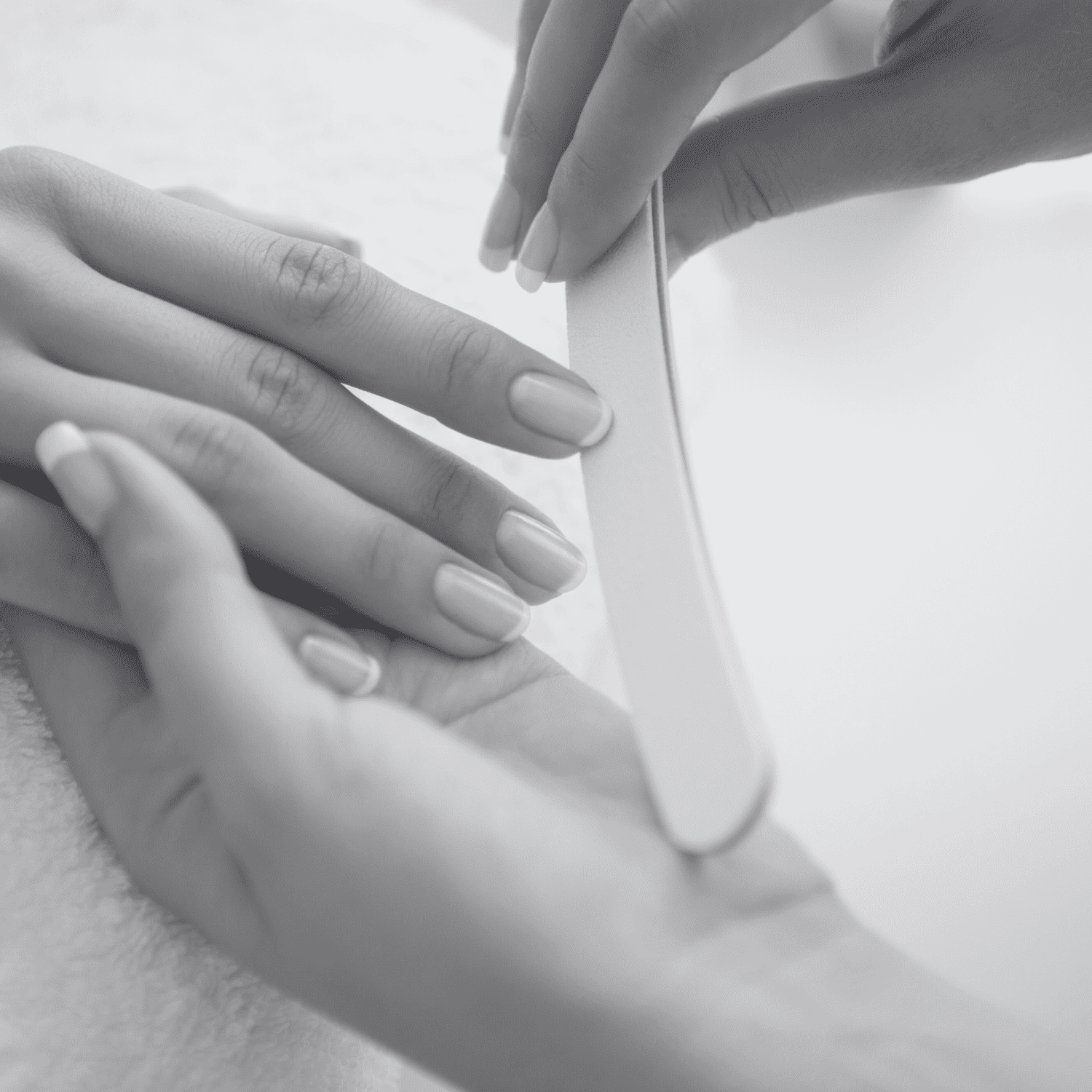 A person receiving a manicure, with focus on nail filing by a professional.