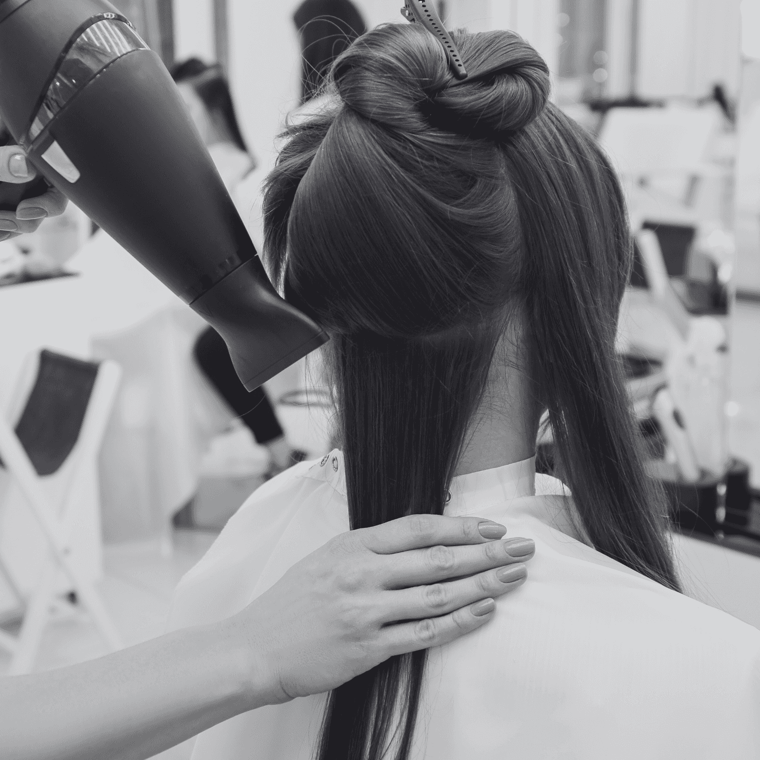 Hairdresser blow-drying a woman's hair in a salon.
